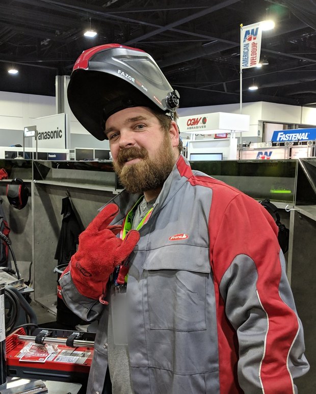 Rob Story in a welding jacket with his hood flipped up, standing at a weld booth.