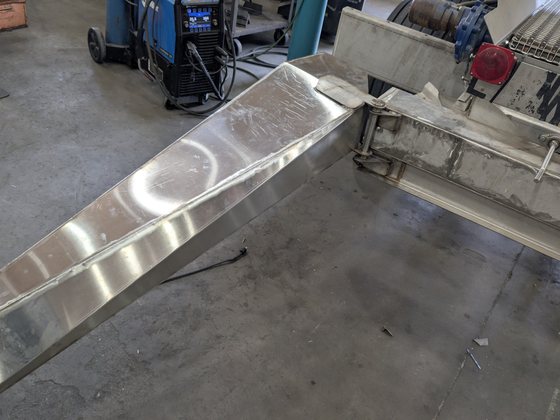 The finished stainless chute hinged out from the machine on a shop floor.