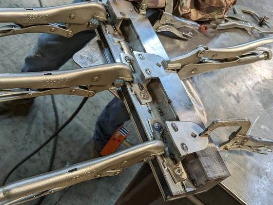Three bearing brackets clamped along the fixture rail with locking pliers, ready to weld.